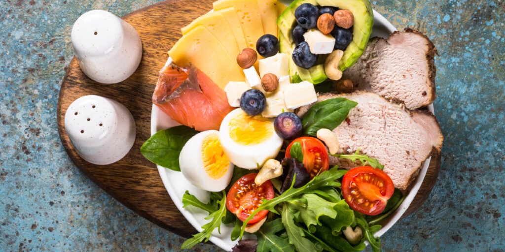 Prato equilibrado com salada, ovo, salmão, carne, fruta e frutos secos