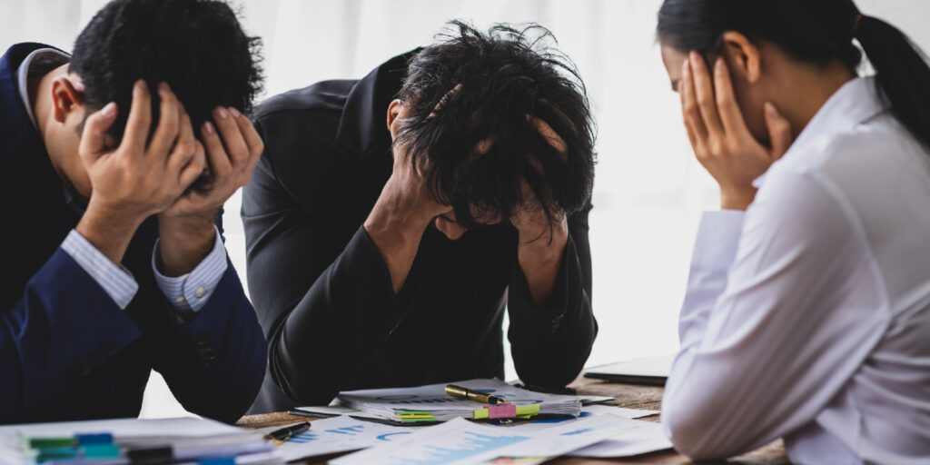 Colegas de trabalho com as mãos na cabeça, cansados e ansiosos