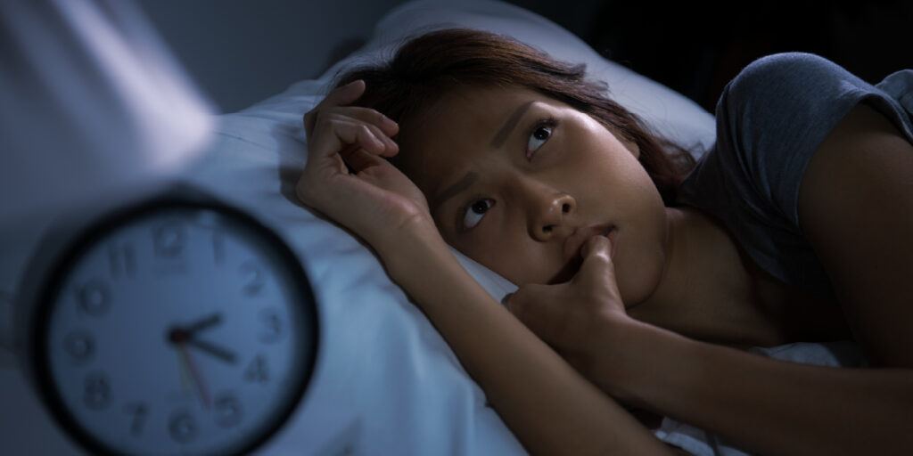 Mulher acordada na cama ao lado de um despertador, sem conseguir dormir